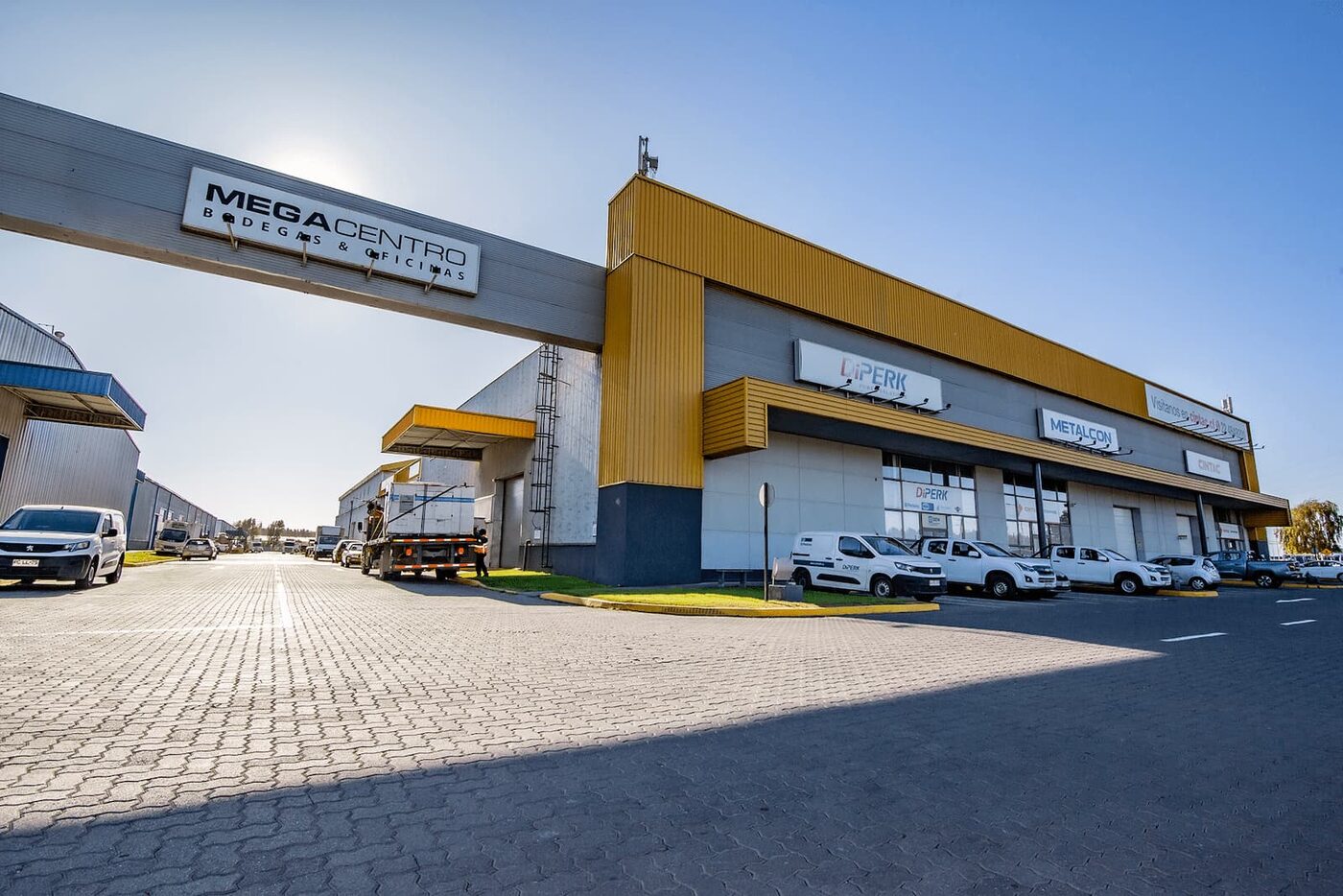 Acceso principal de Megacentro San Pedro con pórtico, locales comerciales y patio de camiones